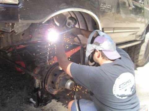 1989 Ford Bronco - A mechanic is welding the suspension of a vehicle, with sparks flying from the welding torch.