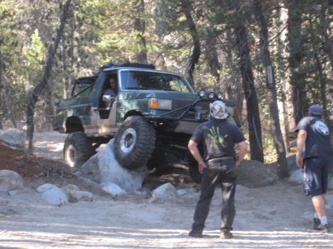 1989 Ford Bronco - An off-road vehicle navigates a rocky trail, with two onlookers observing the challenging terrain.