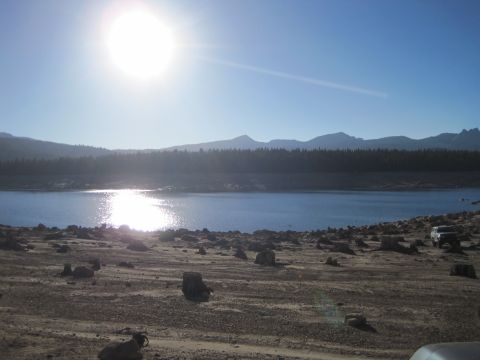 1989 Ford Bronco - A white SUV is parked on a barren, rocky shore next to a calm lake with mountains in the distance.