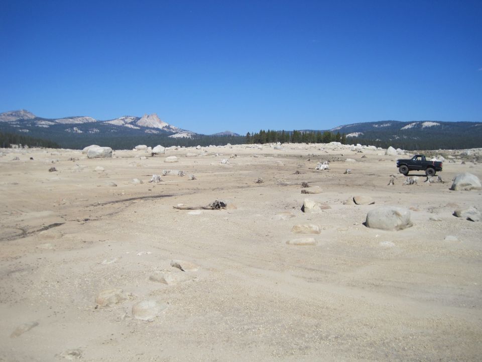 Black pickup truck parked on a dry, rocky plain with mountains in the background