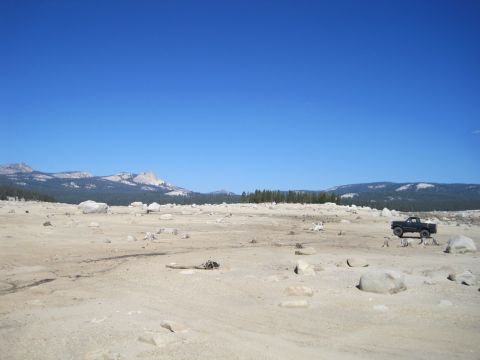 1989 Ford Bronco - A lone black pickup truck sits in a barren, rocky terrain under a clear blue sky, with distant mountains and trees on the horizon.
