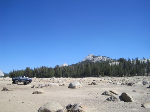 1989 Ford Bronco - A blue pickup truck is parked in a desolate, rocky landscape under a clear blue sky.