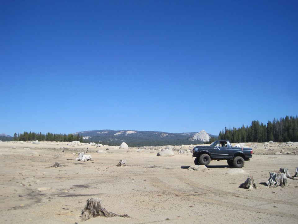 Dark blue 1987 Ford Bronco parked on dry ground with mountains behind
