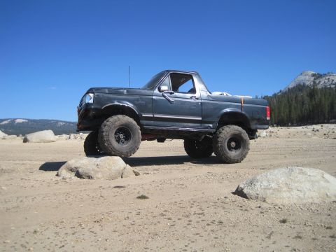 1989 Ford Bronco - A lifted Ford Bronco navigates rocky terrain under a clear blue sky.