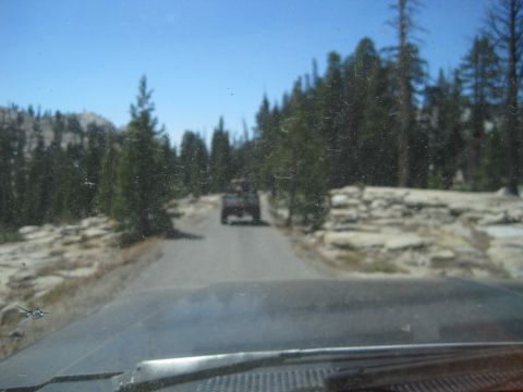 1989 Ford Bronco - A dark SUV is seen from behind driving on a road surrounded by trees and rocks.