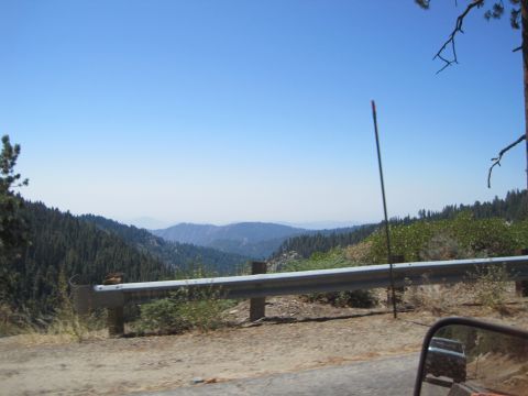 1989 Ford Bronco - A scenic view of rolling hills and dense forests, bordered by a metal guardrail, under a bright blue sky.