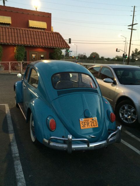 1968 Ford Mustang - A blue Volkswagen Beetle is parked in a lot next to another vehicle, with a building in the background.