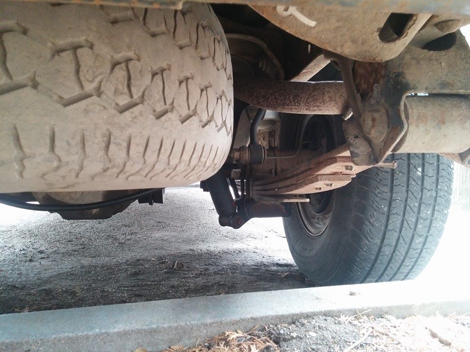 Underside view of a vehicle's rear suspension with leaf springs, shock absorber, and spare tire visible