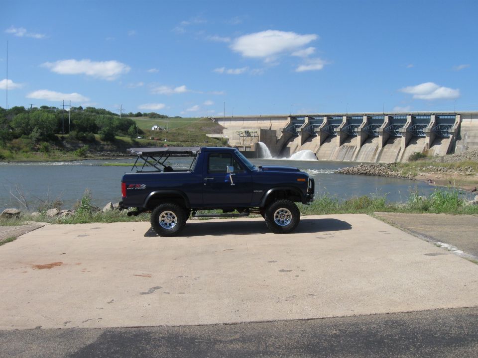 Dark blue Ford Bronco parked on concrete near a dam, side view