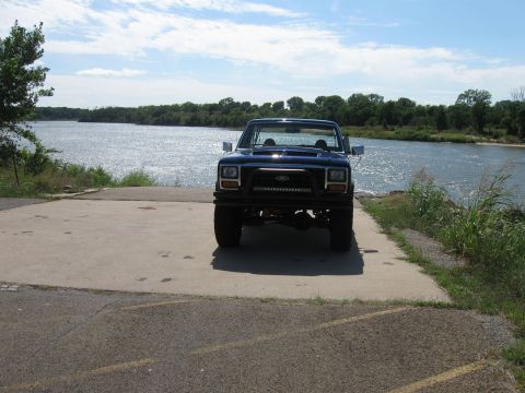 1982 Ford Bronco - Ford Bronco sits on a concrete boat ramp next to a large body of water under a partly cloudy sky.