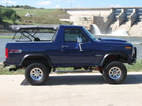 1982 Ford Bronco - This lifted Bronco features an FX4 off-road decal and a removable soft top, parked in front of a large dam.