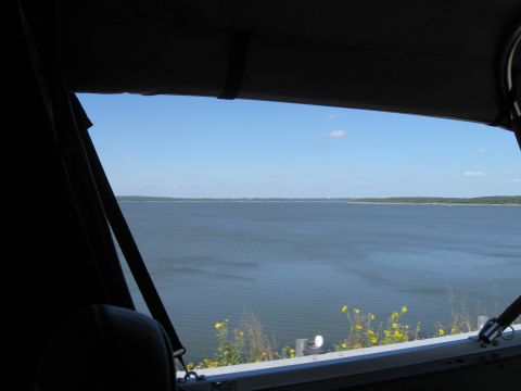 1982 Ford Bronco - View from inside a vehicle shows a calm lake and distant tree line under a bright blue sky.