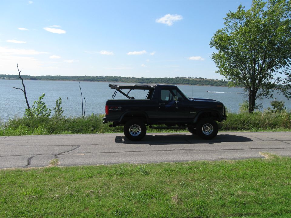 Black 1982 Ford Bronco with soft top driving by a lake