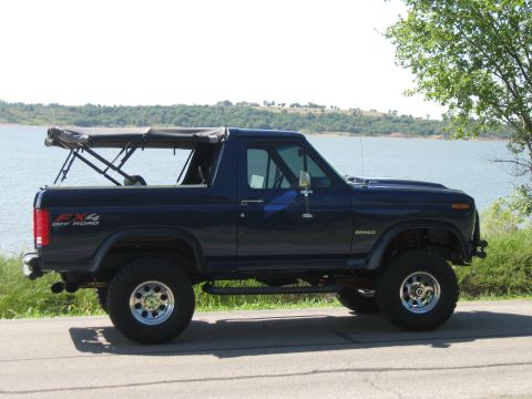 1982 Ford Bronco - This 1982 Ford Bronco is shown in a side profile, parked near a large body of water with its soft top removed.