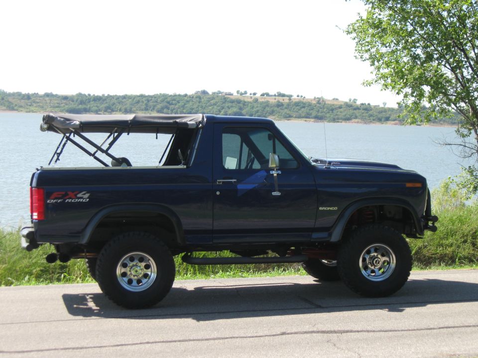 1982 Ford Bronco side view, dark blue with soft top down, parked by water