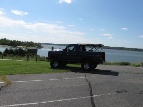 1982 Ford Bronco - Dark colored 1982 Ford Bronco parked near a body of water under a partly cloudy sky.