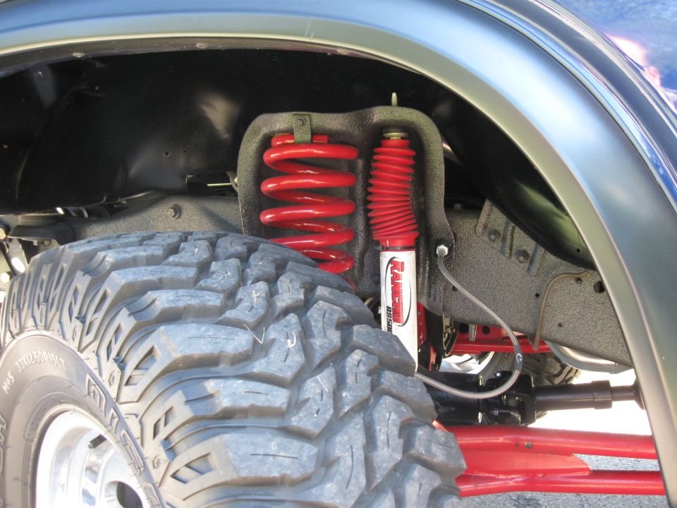 Close-up of a large off-road tire and red coilover suspension with a white Rancho shock absorber
