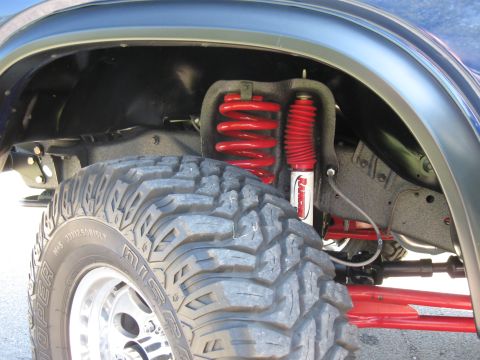 1982 Ford Bronco - Close-up of the front suspension system, red coilover shocks and a large off-road tire.