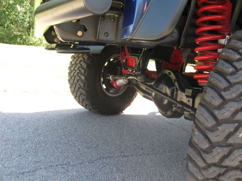 1982 Ford Bronco - Close-up view of the front axle and suspension system of a blue SUV with aftermarket modifications.