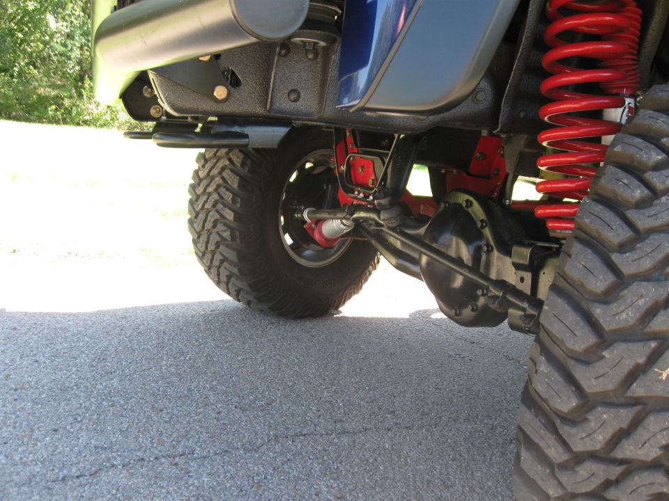 Blue SUV's front axle, red coil springs, and large tire on asphalt