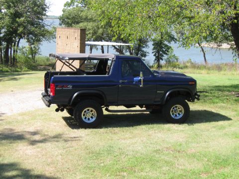 1982 Ford Bronco - This dark blue Ford Bronco is seen from a three-quarter front angle, parked outdoors with a lake in the background.
