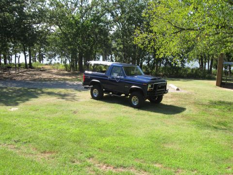 1982 Ford Bronco - This lifted Ford Bronco sits in a grassy area with trees and water in the background.