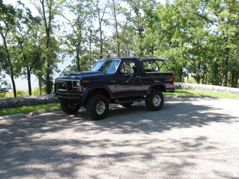 1982 Ford Bronco - This lifted 1982 Ford Bronco is parked on a gravel lot with trees and water in the background.