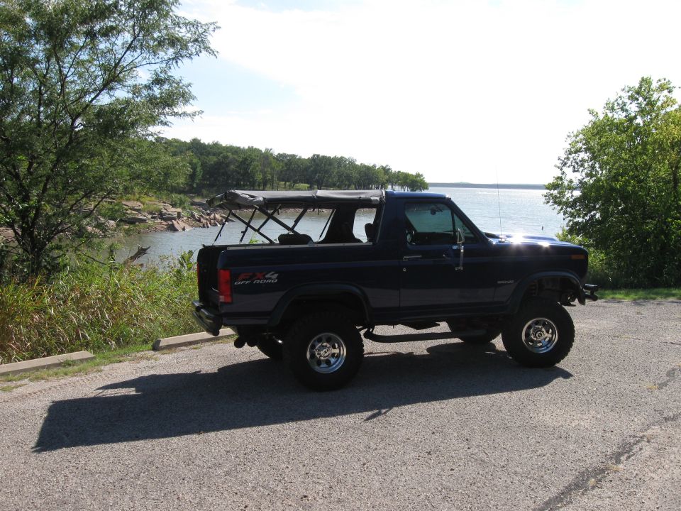 Dark blue Ford Bronco parked by a lake with the top down