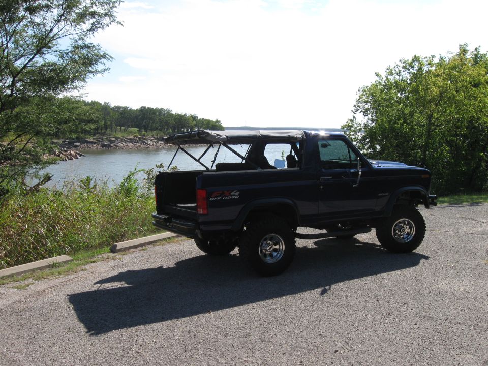 Dark blue Ford Bronco with a soft top, lifted suspension, and off-road tires parked by a lake