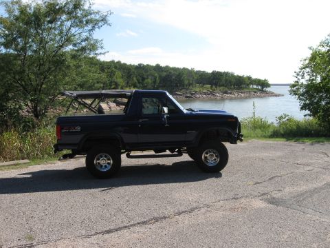 1982 Ford Bronco - This 1982 Ford Bronco is seen parked on a paved surface next to a body of water with trees in the background.