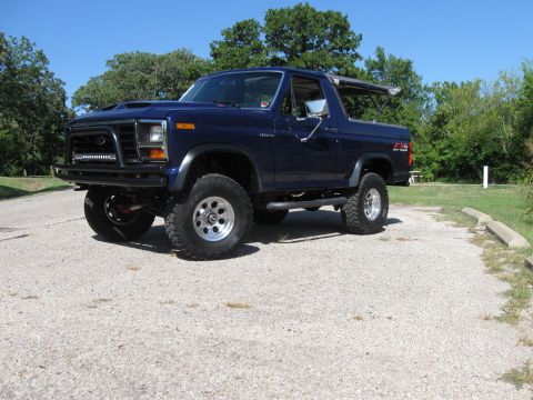 1982 Ford Bronco - This modified Ford Bronco sits parked on a gravel lot under a clear blue sky.