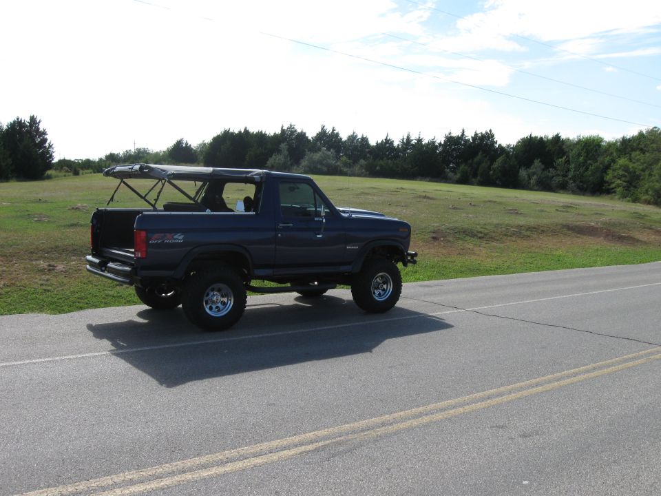 Blue Ford Bronco with soft top removed, driving on a road