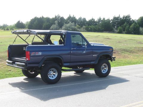 1982 Ford Bronco - This blue Ford Bronco, likely from the early 1980s, is shown with its soft top removed, revealing its interior and lifted off-road suspensi…