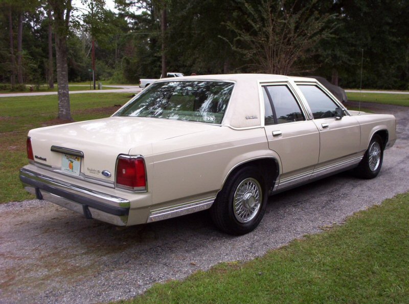 Rear 3/4 view of a beige 1990 Ford Crown Victoria LTD parked on a gravel driveway