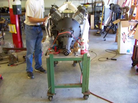 1974 Dodge Challenger - A V8 engine is mounted on a green rolling stand in a garage setting, with a person standing nearby.