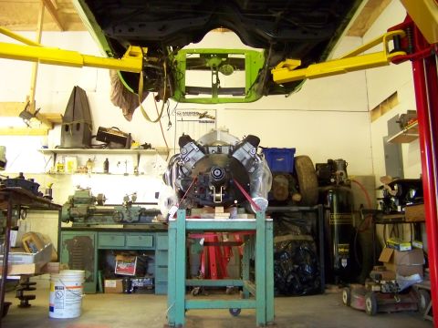 1974 Dodge Challenger - An engine is prepared for installation in a garage setting, with the vehicle body suspended overhead.
