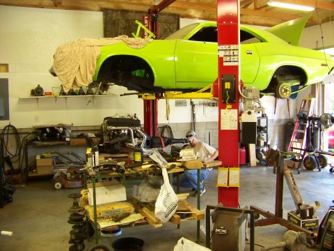 1974 Dodge Challenger - A lime green muscle car is suspended on a lift in a garage, with its engine removed and various tools and parts scattered around.