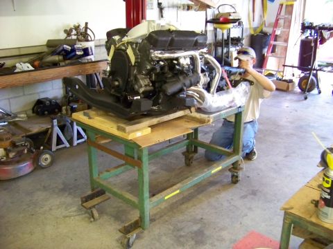 1974 Dodge Challenger - A person works on an engine that is mounted on a rolling cart in a workshop.