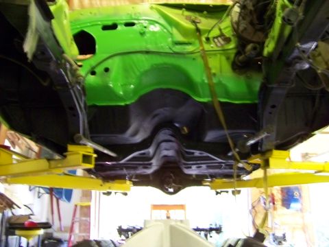 1974 Dodge Challenger - Underside view of a 1974 Dodge Challenger's engine bay, painted bright green and suspended on a yellow lift.