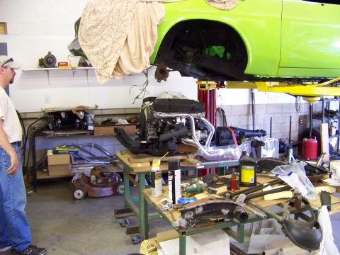 1974 Dodge Challenger - A car is suspended on a lift while its engine sits on a table, surrounded by tools and parts.