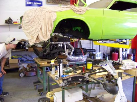 1974 Dodge Challenger - Engine installation in progress on a lime green 1974 Dodge Challenger, with the vehicle raised on a lift in a garage.