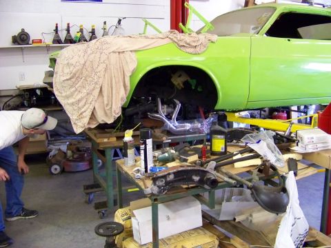 1974 Dodge Challenger - A mechanic inspects the underside of a car undergoing repairs in a cluttered garage.