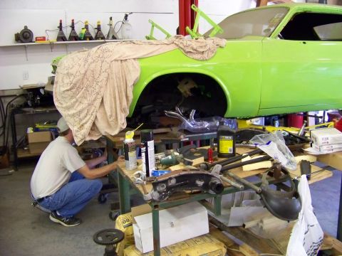 1974 Dodge Challenger - A mechanic works on a lime green 1974 Dodge Challenger that is raised on a lift in a garage.