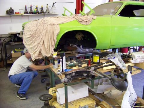 1974 Dodge Challenger - A mechanic works on the engine of a bright green 1974 Dodge Challenger, which is raised on a lift in a workshop.