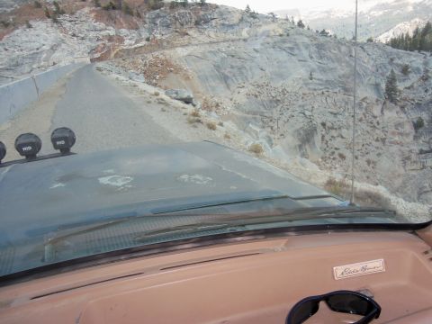 1968 Ford Bronco - View from inside a vehicle as it navigates a mountain road, with off-road lights visible on the roof.