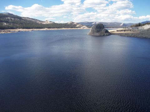 1968 Ford Bronco - A vast blue lake stretches out towards distant hills, with a prominent rock formation rising from the water.