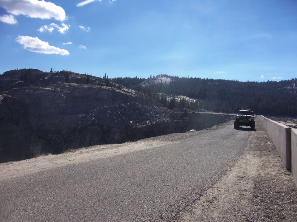 Black 1968 Ford Bronco driving on a road with a rocky hillside