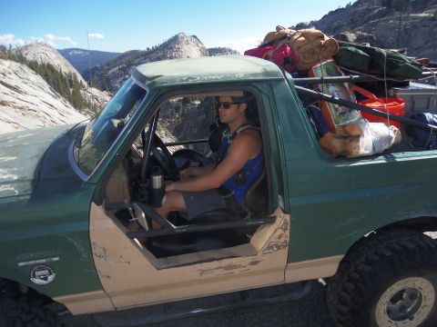 1968 Ford Bronco - Man drives a heavily loaded off-road vehicle through a mountainous landscape.