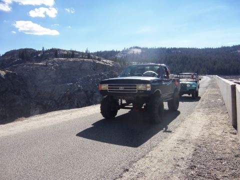 1968 Ford Bronco - Two off-road vehicles travel along a paved road with a scenic mountain landscape.