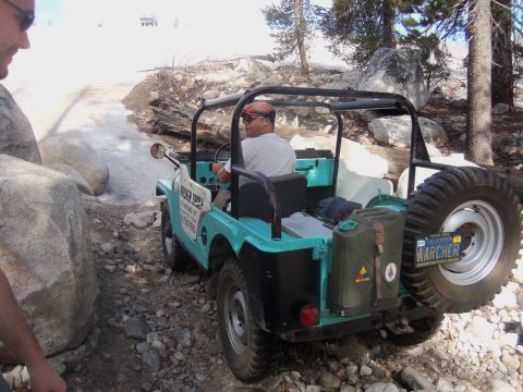 1968 Ford Bronco - A teal Jeep CJ-5 navigates a rocky trail, with a spare tire mounted on the back and a jerry can attached.
